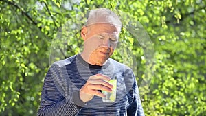 An elderly man puts a yellow soluble tablet in a glass of water against a background of spring greenery