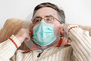 Elderly man putting a medical mask on his face to protect himself from coronavirus pandemic.