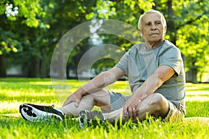Elderly man relaxing in green city park after his workout