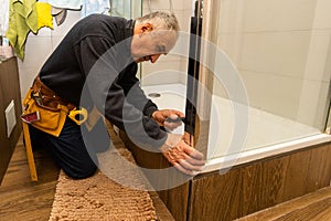 an elderly man repairing door of shower cabin in bathroom