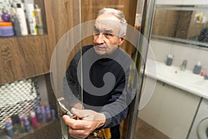 an elderly man repairing door of shower cabin in bathroom
