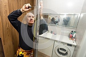 an elderly man repairing door of shower cabin in bathroom