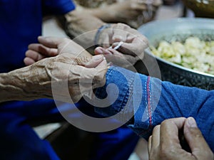 Elderly man`s hands waving a white string  Sai Sin  around younger one`s hands - Thai traditional blessing from an elder one