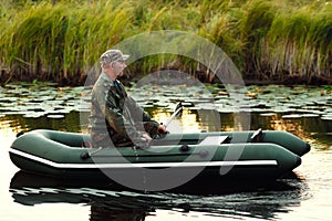 An elderly man is sailing on a rubber boat with oars on a calm river. The inspector checks the reservoir from poachers