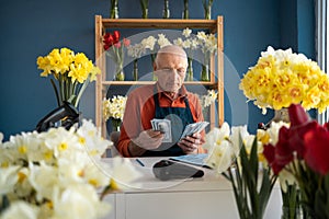 Elderly man seller florist sitting counting money for sold flowers.