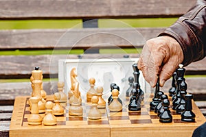 Elderly man senior holds chess piece game board outdoors