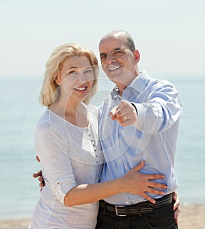 Elderly man showing something hand an woman on the beach