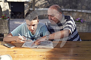 A elderly man sitting doing crosswords hobby with his grandson