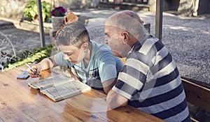 A elderly man sitting doing crosswords hobby with his grandson