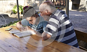 A elderly man sitting doing crosswords hobby with his grandson