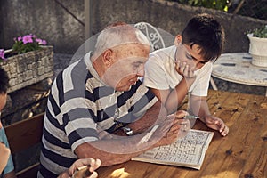A elderly man sitting doing crosswords hobby with his grandson