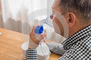 Elderly man sitting on a table and using a nebulizer mist at home