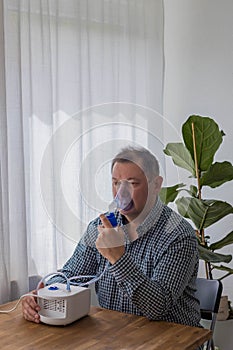 Elderly man sitting on a table and using a nebulizer mist at home