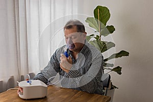 Elderly man sitting on a table and using a nebulizer mist at home