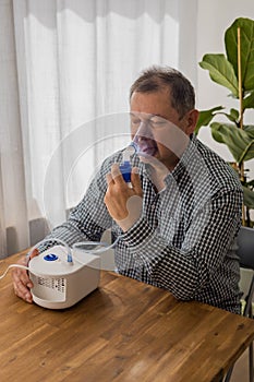 Elderly man sitting on a table and using a nebulizer mist at home