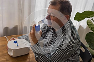 Elderly man sitting on a table and using a nebulizer mist at home