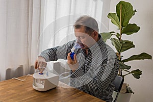 Elderly man sitting on a table and using a nebulizer mist at home