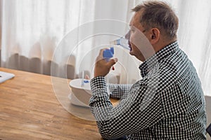 Elderly man sitting on a table and using a nebulizer mist at home