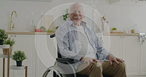 Elderly man sitting in wheelchair in kitchen at home looking at camera during retirement