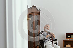 Elderly man sitting on a wheelchair and supporting himself with cane