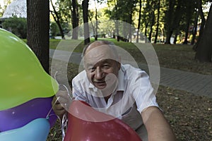 An elderly man with a smile on his face and bright balloons makes a selfie in the park