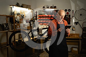 Elderly man standing alone in his bicycle workshop and using technology.
