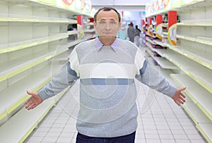 Elderly man stands between empty shelves in shop