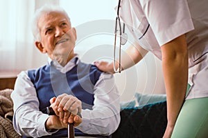 Elderly man with stick being comforted by doctor in nursing home