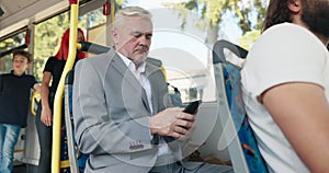 Elderly man in suit rides public transport bus, writes messages on phone, browses articles, journey