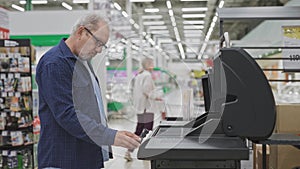 An elderly man in a supermarket chooses an electric barbecue grill. A pensioner in a shop