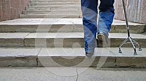 Elderly man with support cane steps up stairs