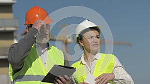 Elderly man with a tablet in his hands and a young woman at a construction site. Builders have fun discussing work