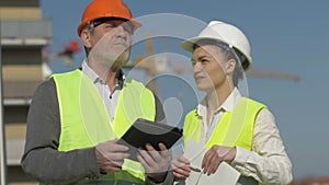 Elderly man with a tablet in his hands and a young woman at a construction site. Builders have fun discussing work