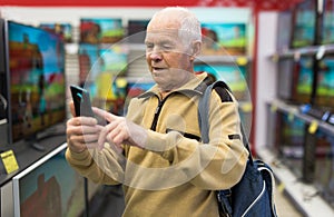 elderly man takes a photo TV in showroom of electronics store