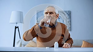 elderly man taking medication and drinking