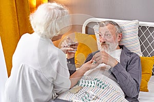 elderly man taking medicines and drinking water while lie on bed, wife help and support