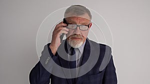 Elderly man talking by mobile phone on white background. Portrait of old caucasian businessman using smartphone for