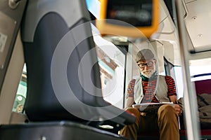 Elderly man traveling through the city by bus, reading newspaper. Senior city commuter taking tram to grocery, using