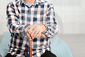 Elderly man with walking cane sitting on bed. Space for text