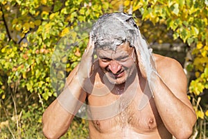 an elderly man washes his hair with shampoo in nature