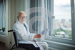 Elderly man in a wheelchair reading the newspaper in his robe in the morning.