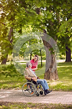 Elderly man in wheelchair talking with daughter in the park- hap