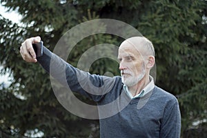 An elderly man with a white beard and bald head makes a selfie