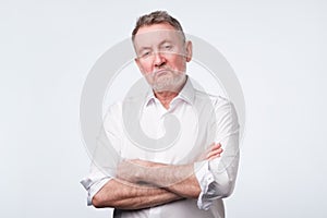 Elderly man in white shirt with his arms crossed looking depressed and annoyed