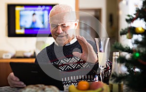 Elderly man wishes Merry Christmas to friends and acquaintances using a laptop