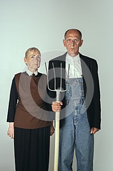 Elderly man and woman in art performance, replica of painting american gothic. Retro style, comparison of eras and