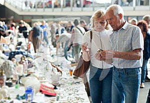 Elderly man and woman consider things in flea market