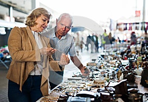 Elderly man and woman consider things in flea market