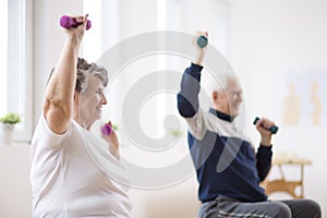 Elderly man and woman exercising with dumbbells during physiotherapy session at hospital