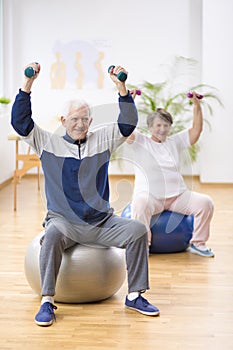 Elderly man and woman exercising on gymnastic balls during physiotherapy session at hospital